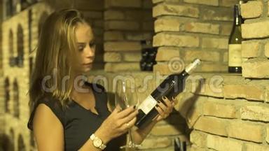 女酿酒师闻着一杯红酒，手拿瓶子在地窖里。 年轻女子品尝红酒